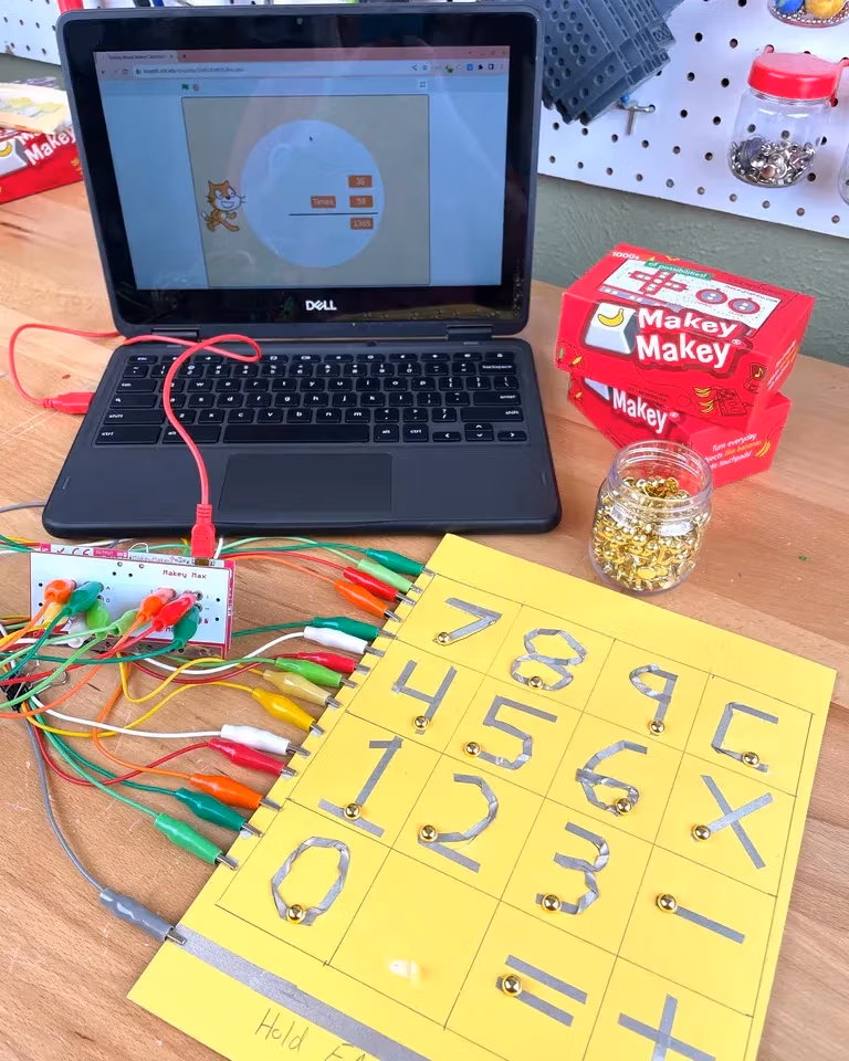 Two hands control a video game using pieces of playdough wired to a laptop.