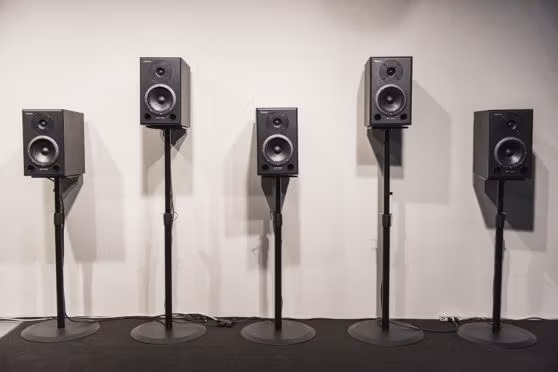 speakers on stands lined up against a blank wall 