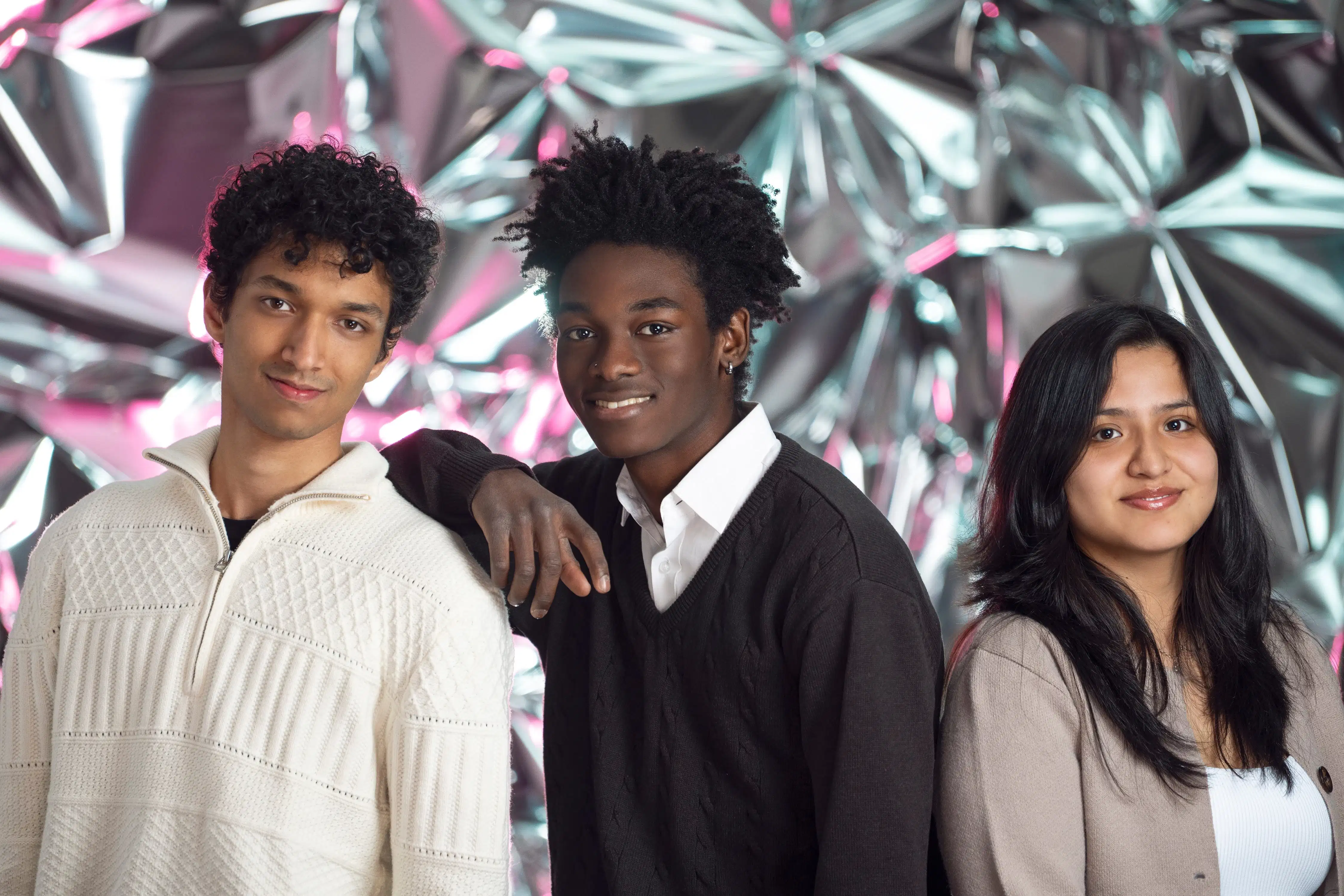 Two guys and a girl smile at the camera in front of a reflective background.
