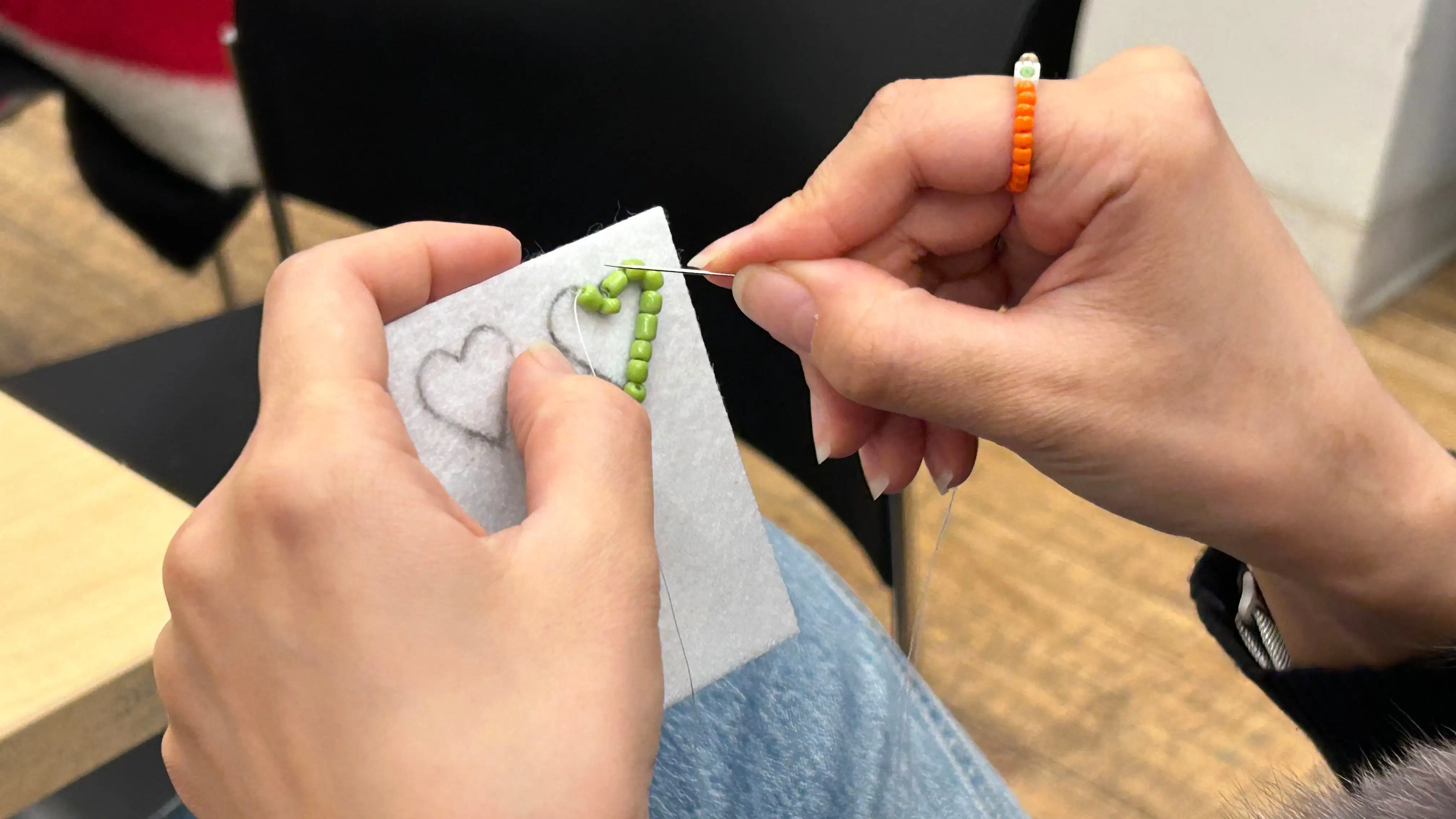 a pair of hands holding felt with a green beaded heart being sewn onto it