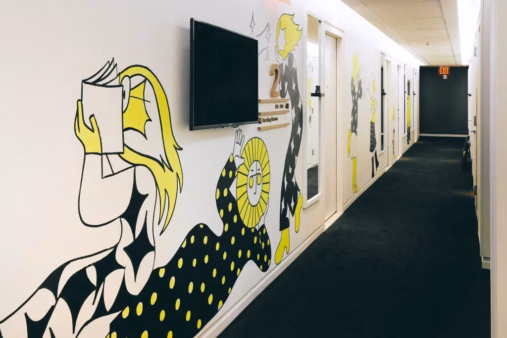 A hall with white walls and a black and yellow mural depicting figures lounging and reading 