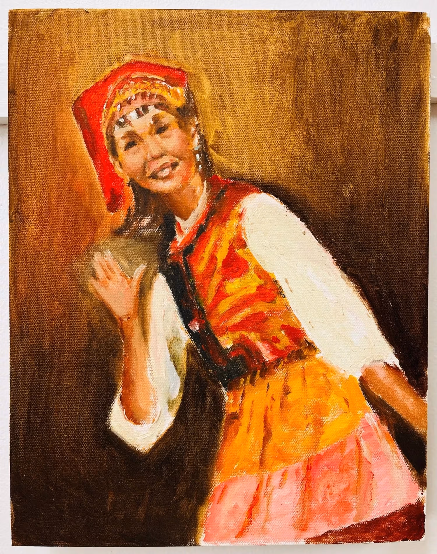 A woman in traditional Yi clothing smiling and waving at the viewer. Her clothes are vibrant in red, yellow, pink, and white with black detailing.