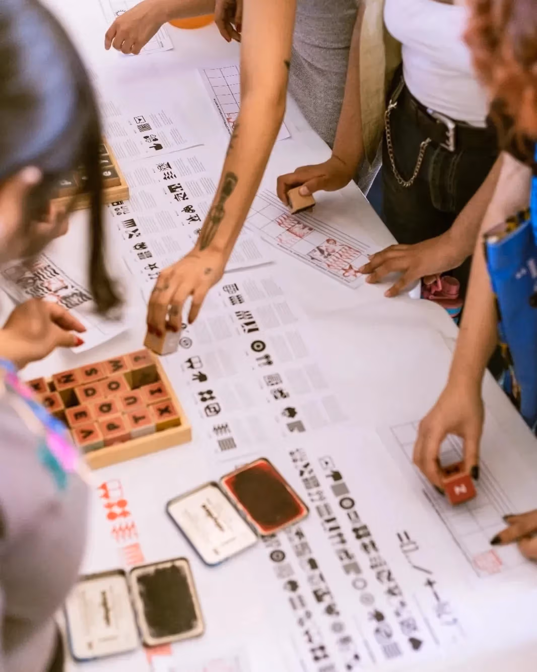 People gather around a table using wooden stamps on paper on a table.