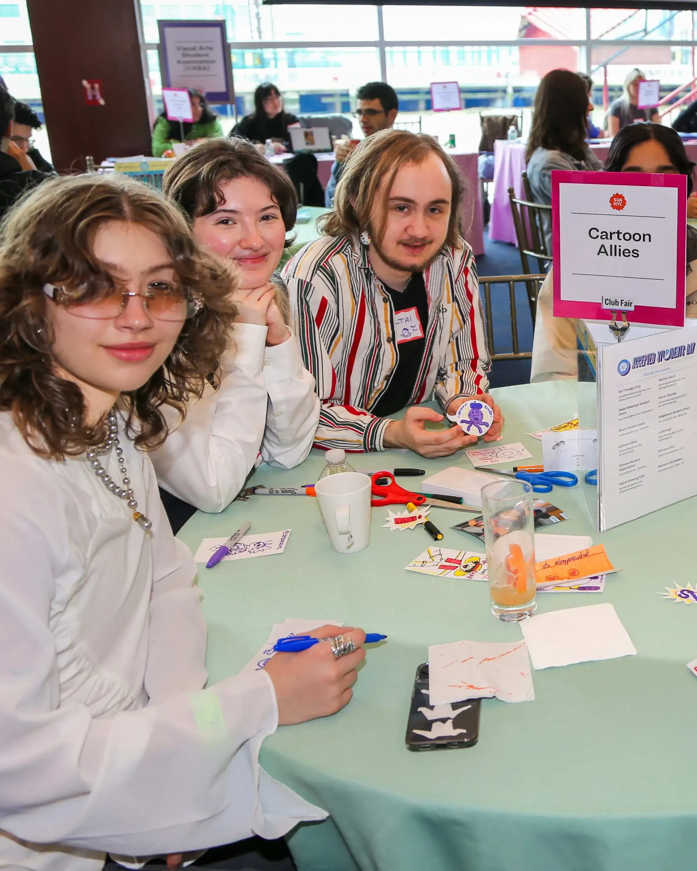 People sitting around a round table at a club fair; a sign in the middle of the table reads “Cartoon Allies”