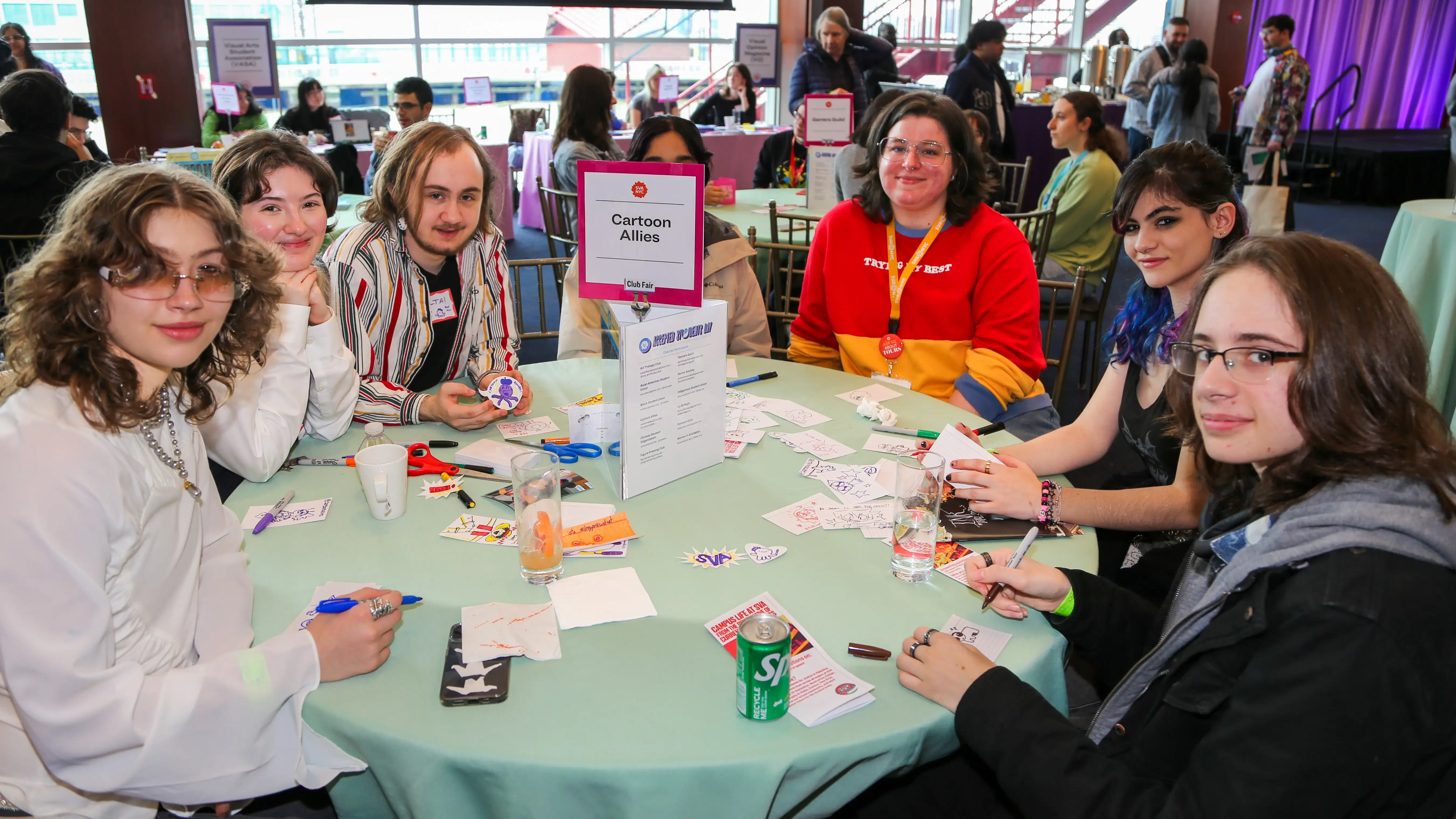 People sitting around a round table at a club fair; a sign in the middle of the table reads “Cartoon Allies”