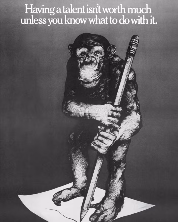 Black and white poster with a chimpanzee holding a large pencil while standing on a sheet of paper.