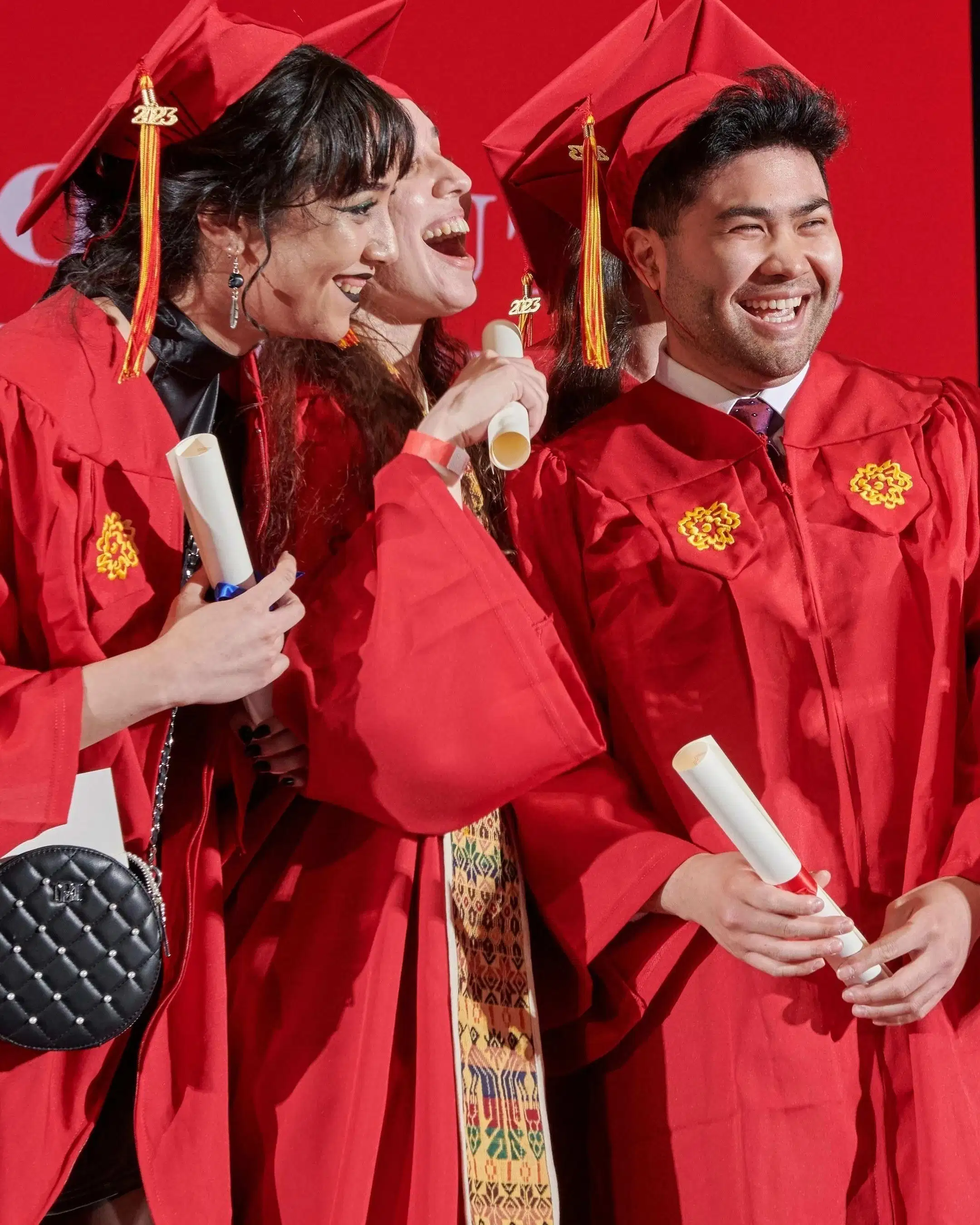 SVA graduating students in red caps and gowns, some holding flowers, smiling and posing for photos inside Radio City Music Hall in New York.