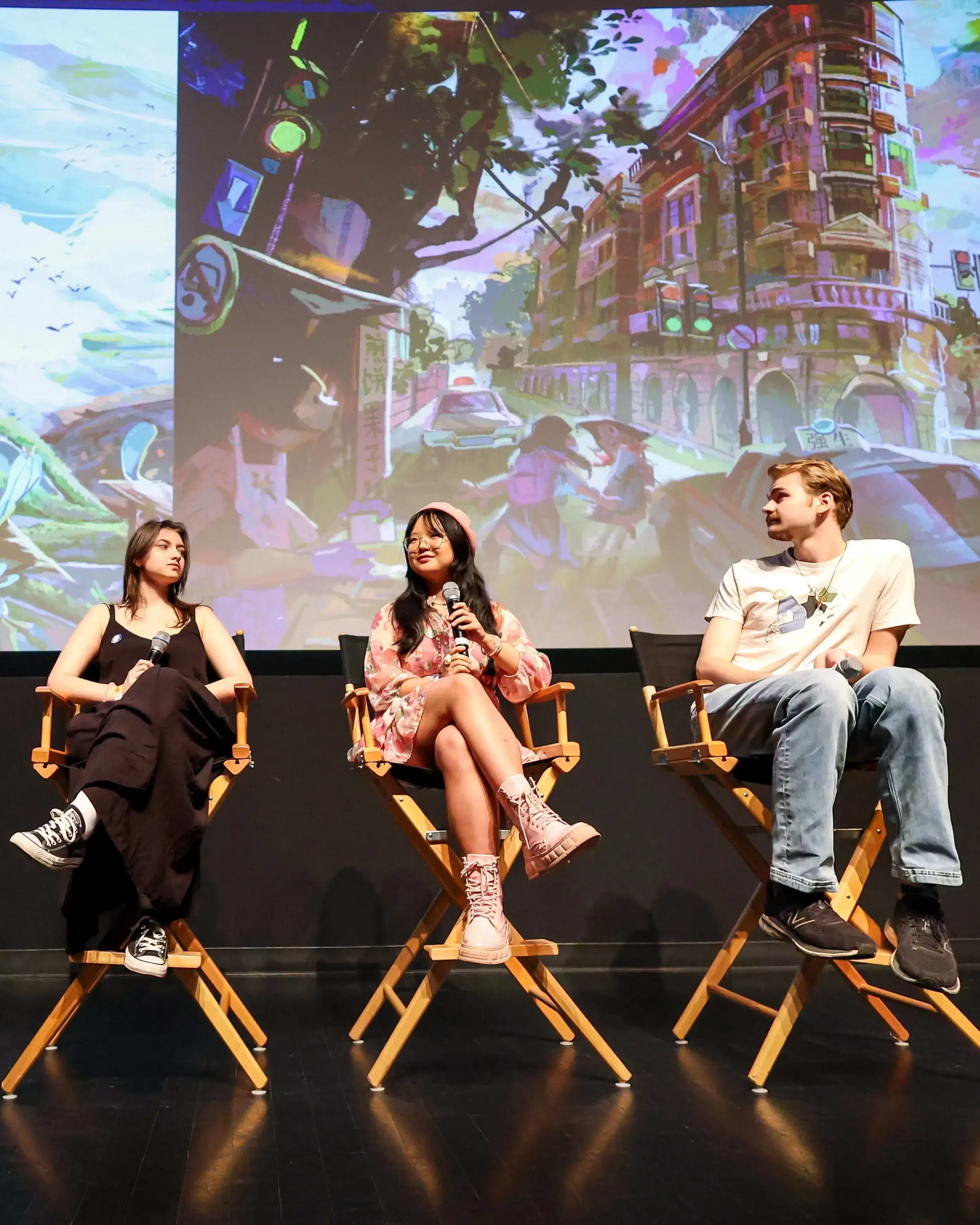 three people sit in director's chairs on stage in front of artwork