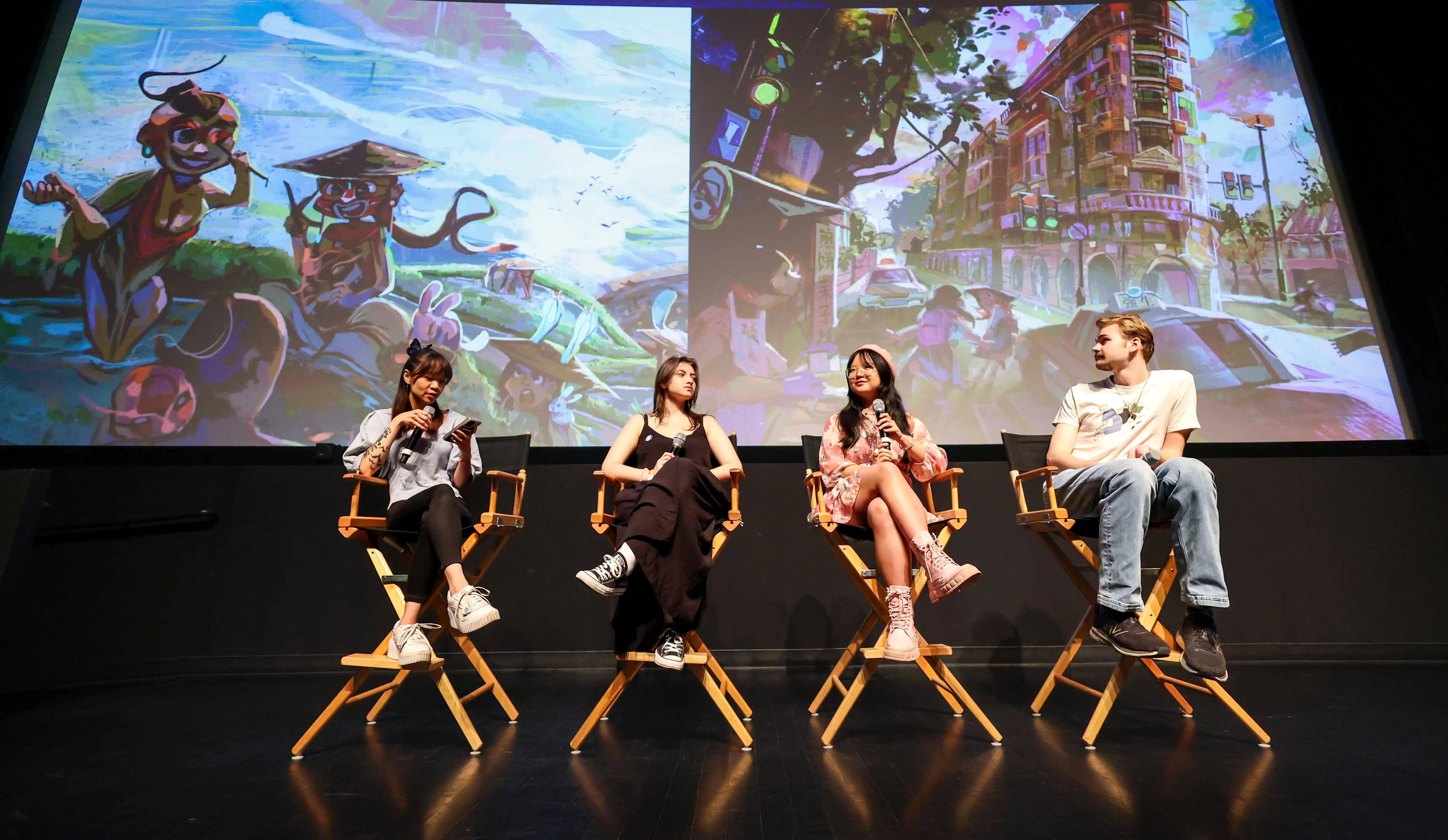 four people sit in director's chairs on stage in front of artwork
