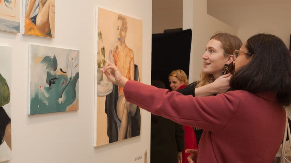 Two students engaging with art mounted on a wall at an exhibition.