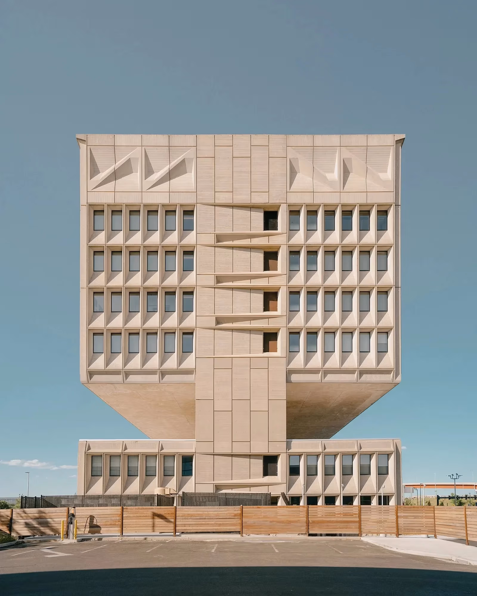 architectural color photo of a large square concrete building against a blue sky.