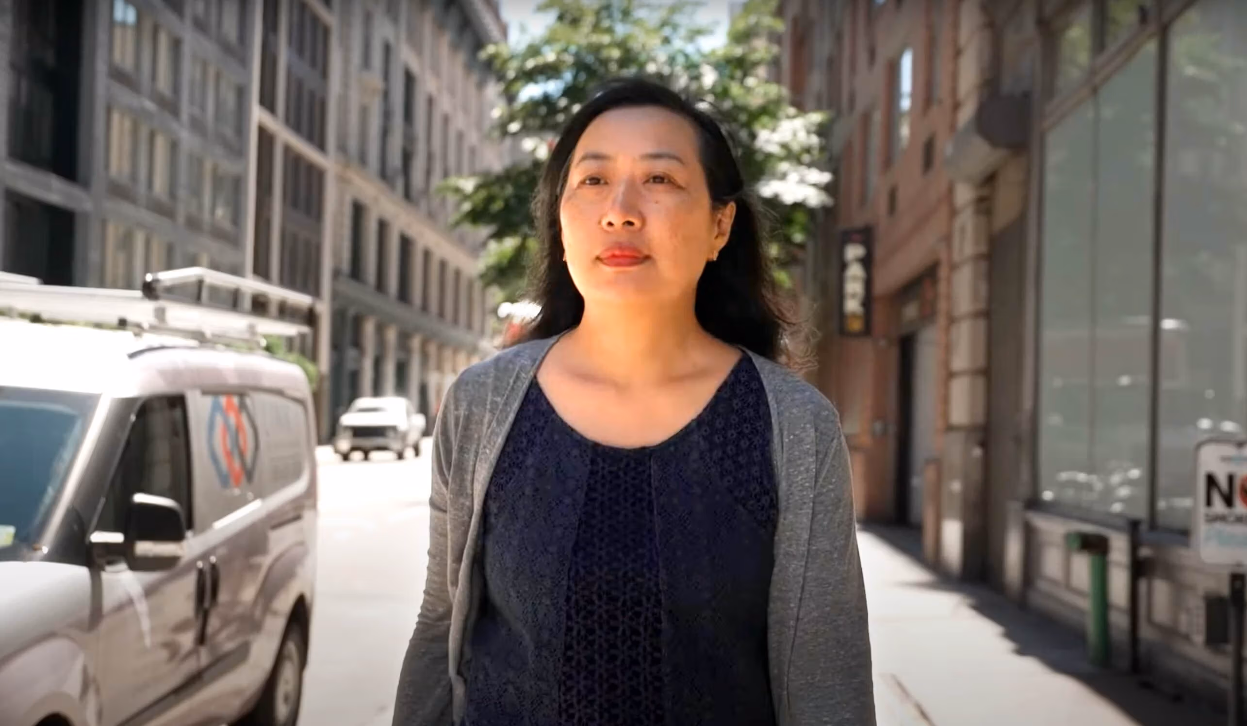 A woman wearing a blue shirt and gray sweater walks down a New York City street on the School of Visual Arts campus.