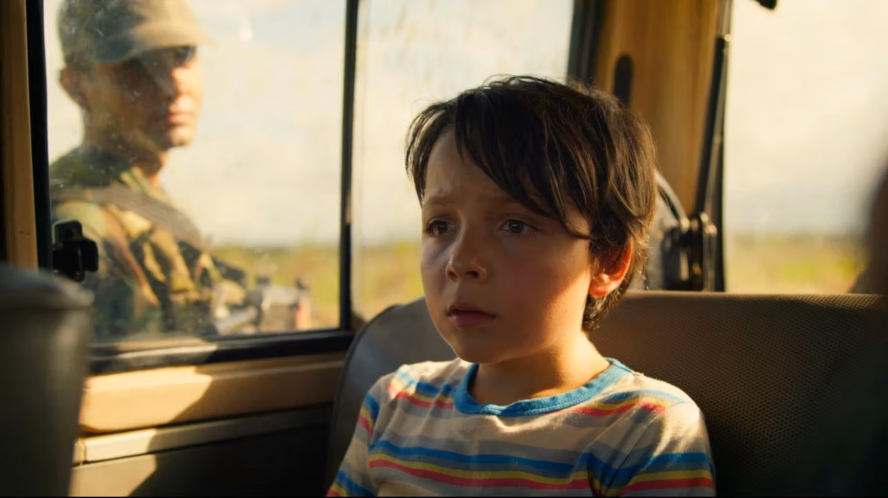  A young boy sitting in the back seat of a vehicle, looking out the window with a thoughtful expression.