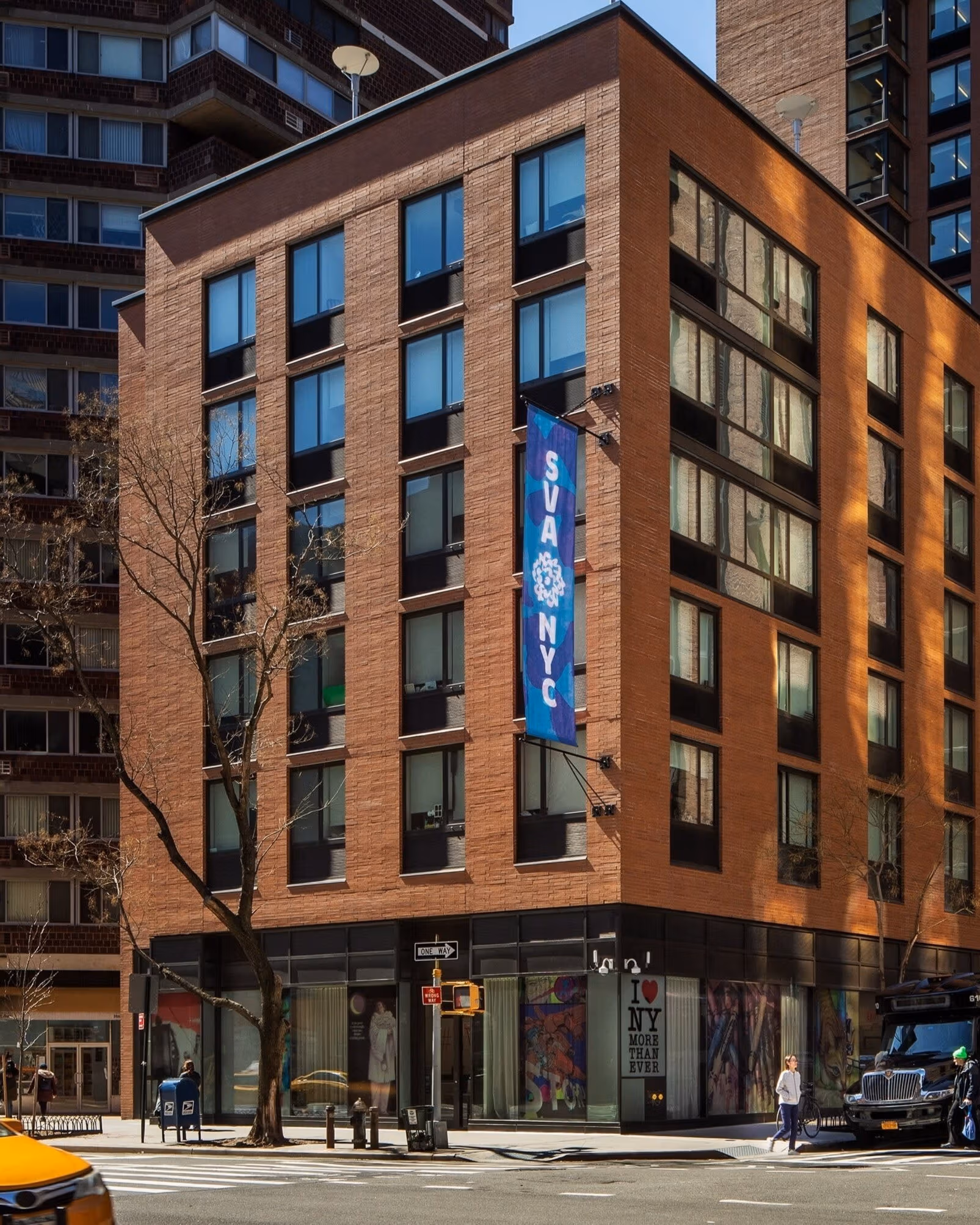 A busy New York City street; a building facade with an ‘SVA’ flag on it.