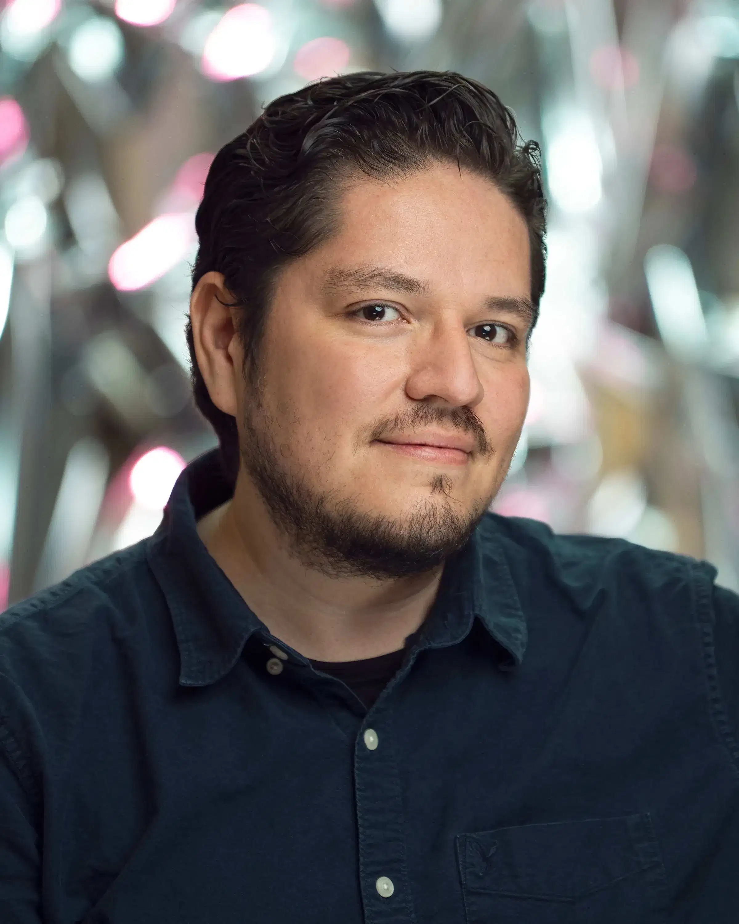 A man in front of a reflective background smiles at the viewer.