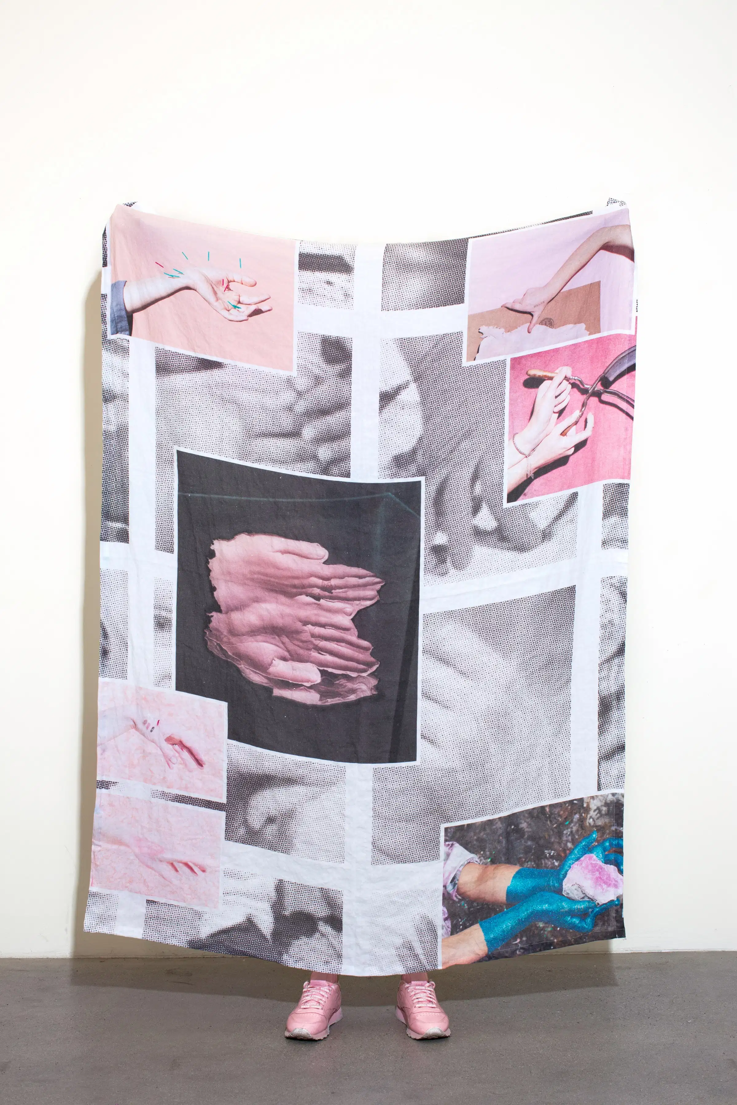 A color photograph of a person holding up a large linen blanket on which many photographs have been printed.