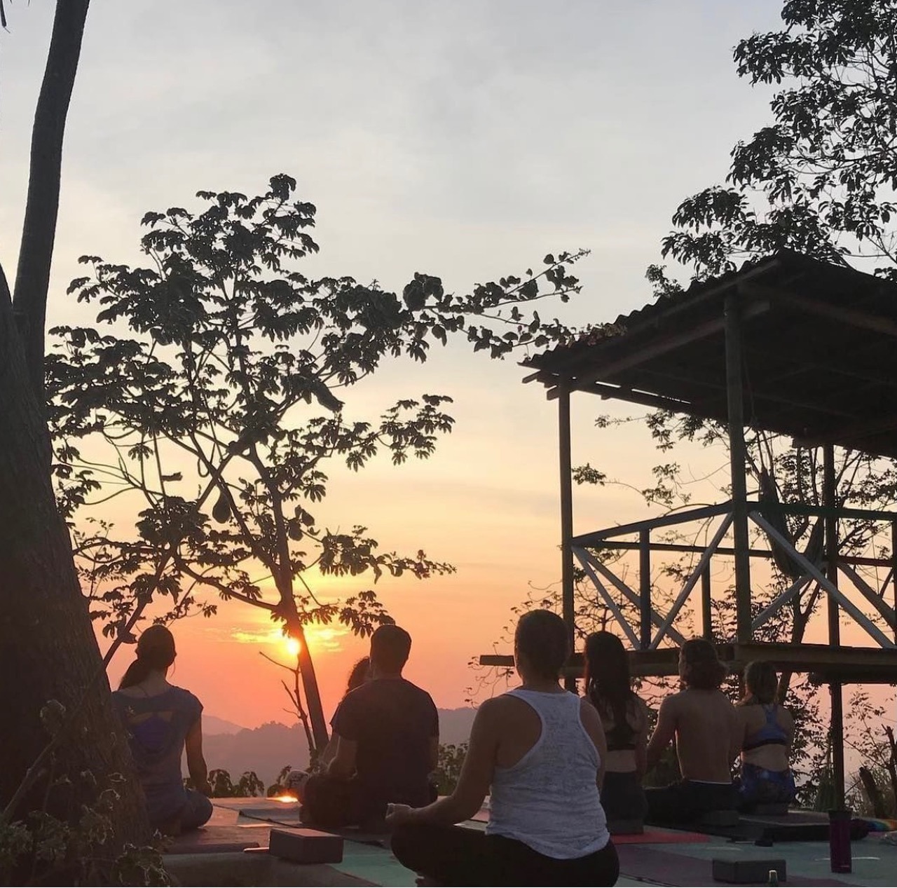 A photo of several people sitting together outdoors during either a sunset or sunrise.