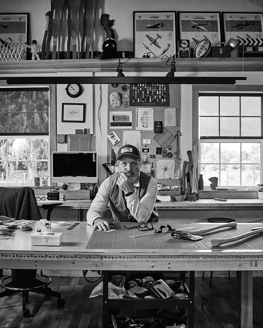 A man working at a desk in a room filled with tools, concentrating on his project in a creative workspace.