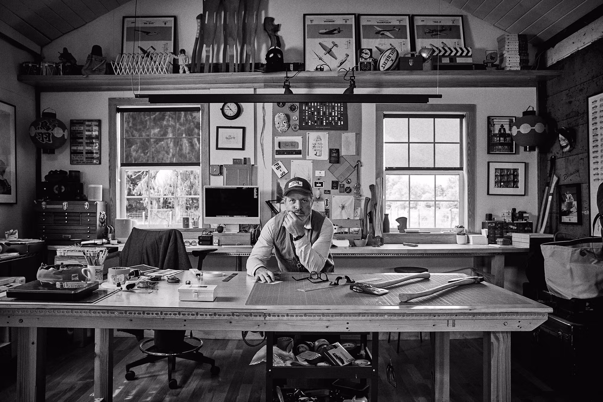 A man working at a desk in a room filled with tools, concentrating on his project in a creative workspace.