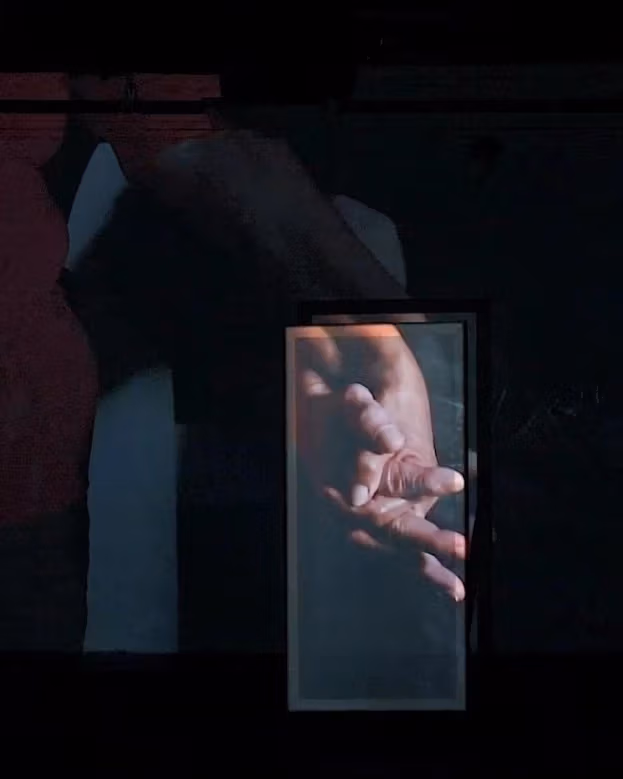 A red room with a black and white painting of a house and more. There is a video being screened in the room on a panel.