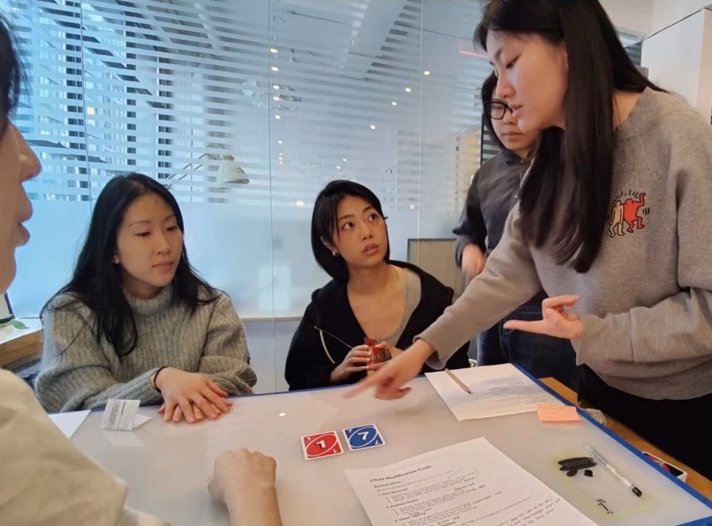 A group of students gathered around a table and discussing the card game Uno.