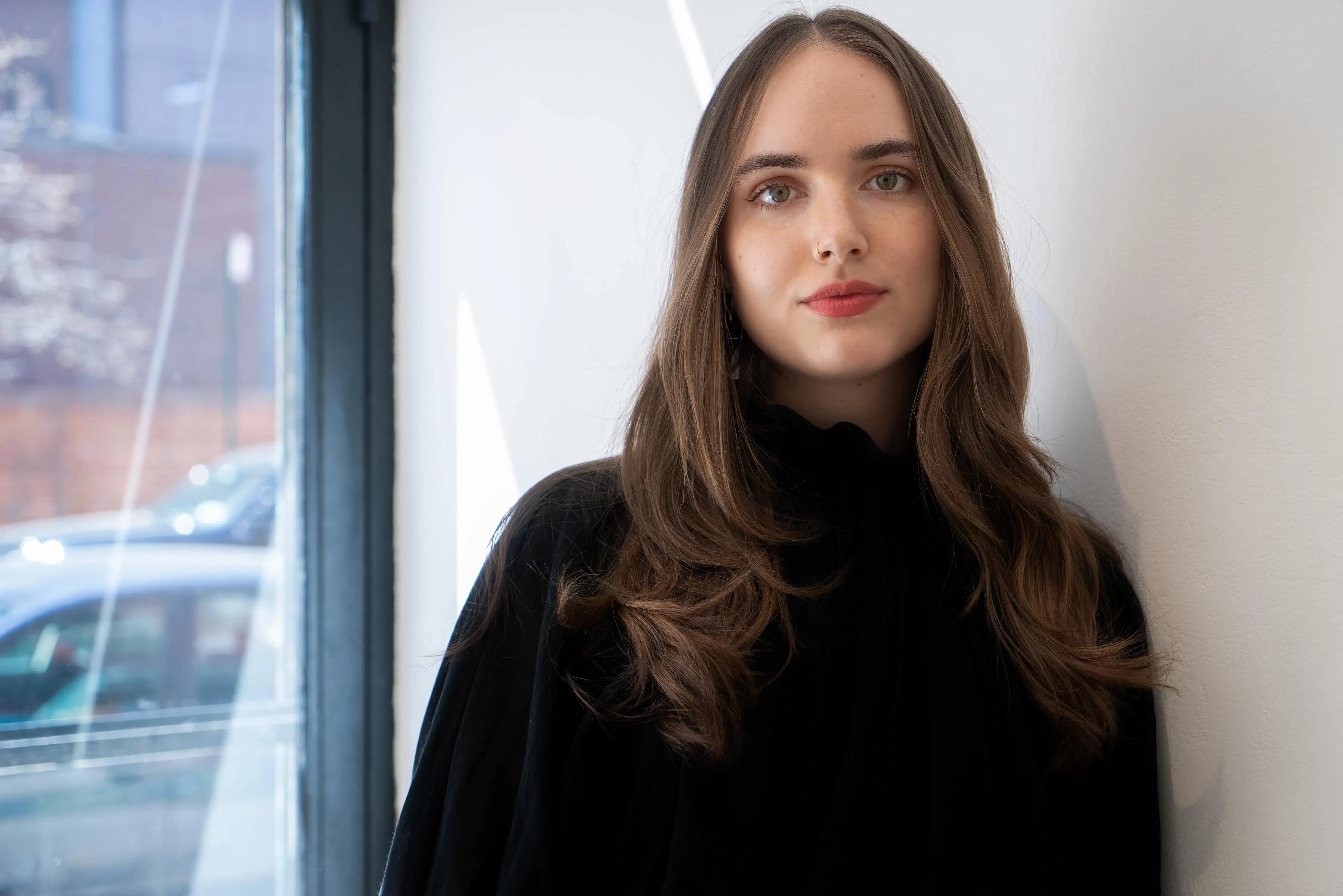 A white woman with light brown hair wearing a black turtle neck stands in front of a white wall.