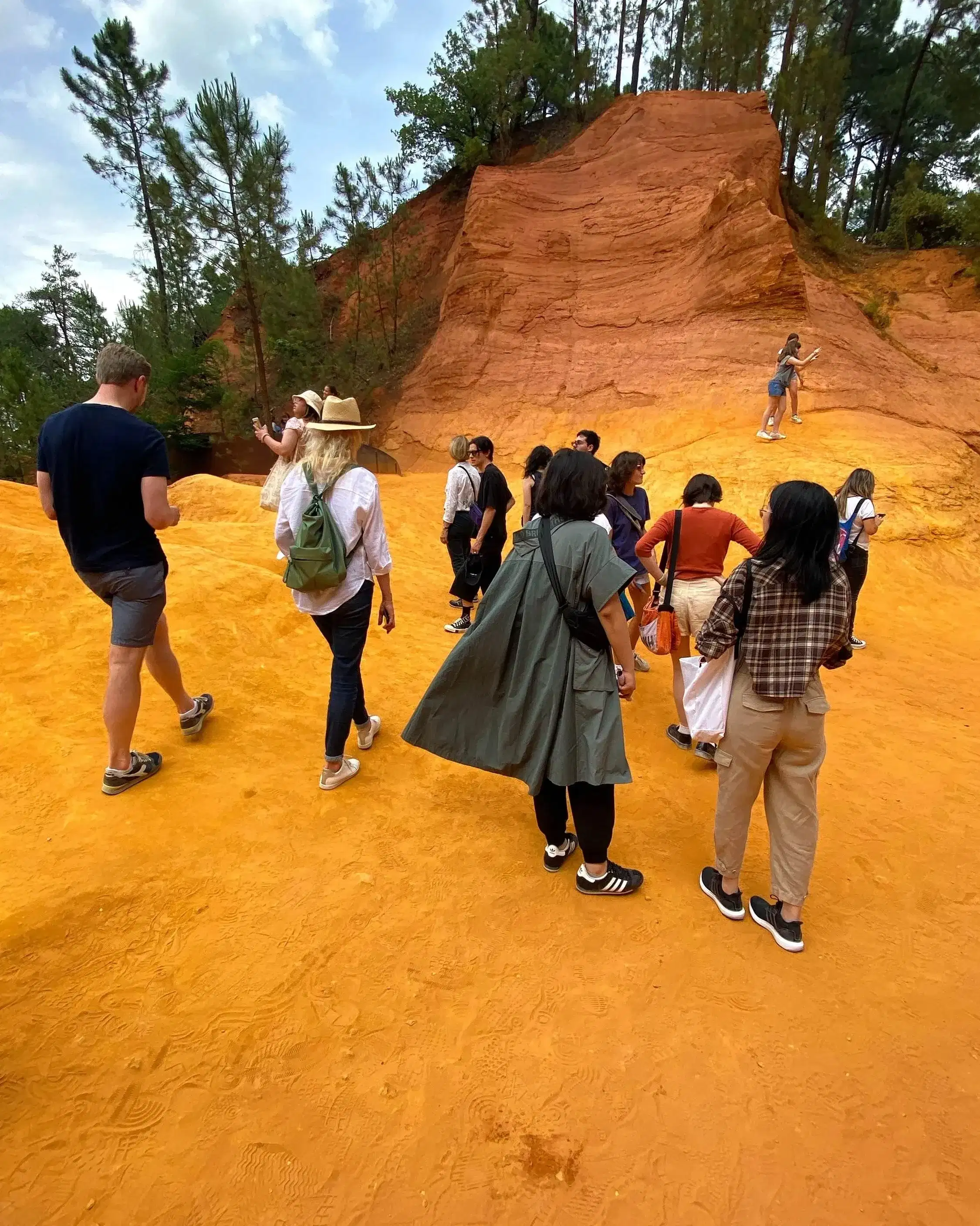 A group of people with cameras and sketchbooks walk on a hike, going up a gorgeously yellowy sandy hill.