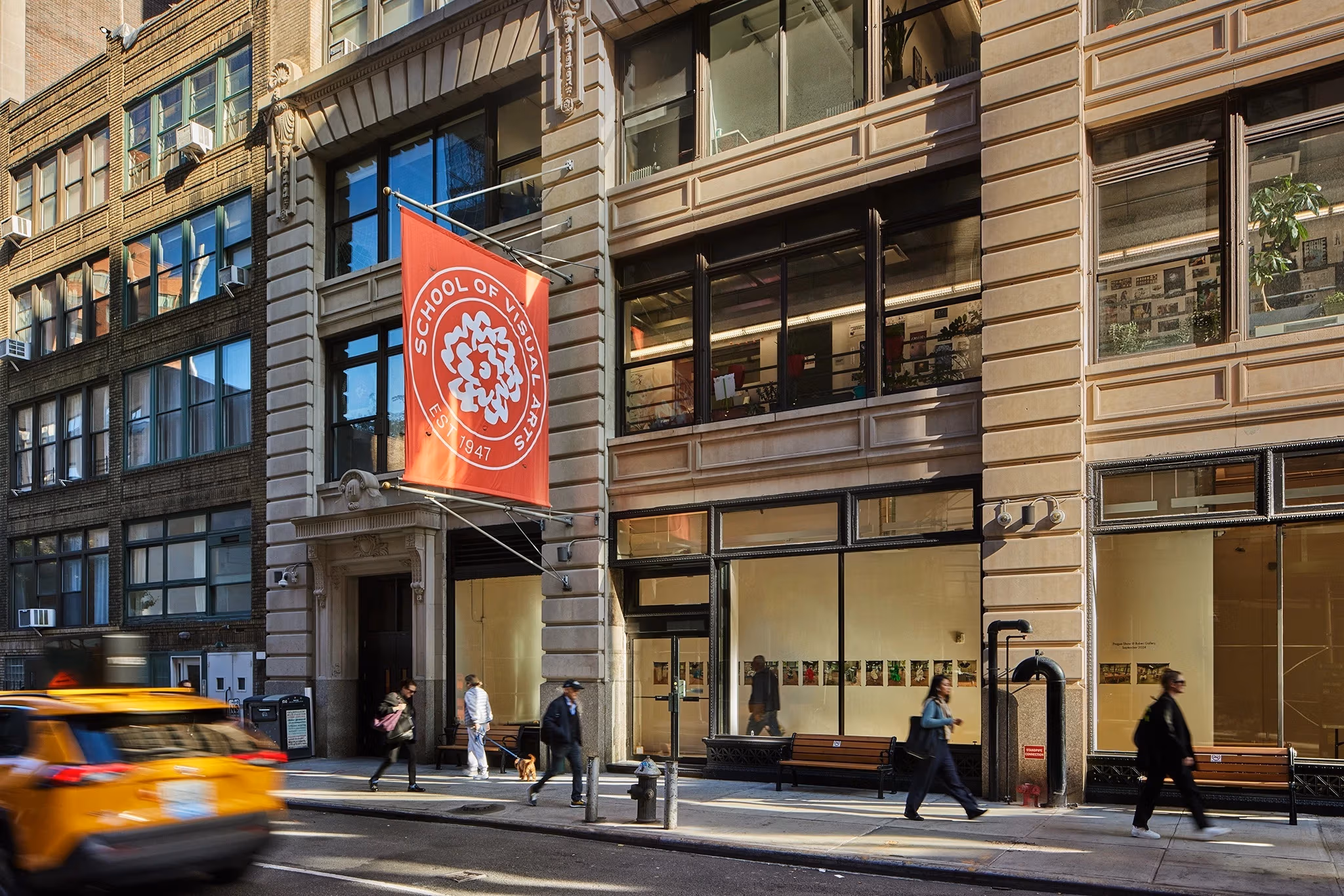 Photograph of the exterior of a tan building in NYC with an orange School of Visual Arts flag out front