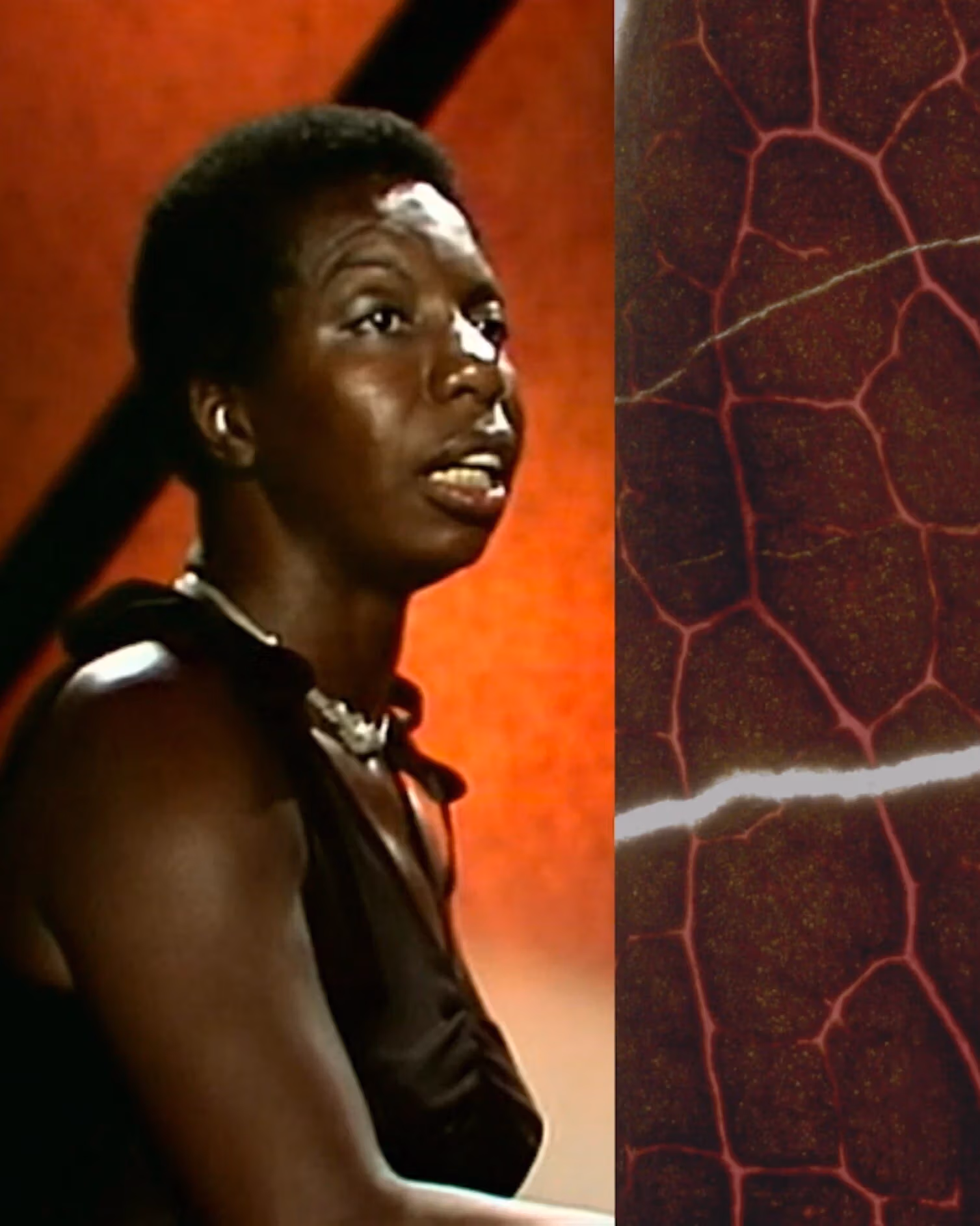 Video still of a woman looking off camera, sitting in an environment mostly composed of deep red tones. 