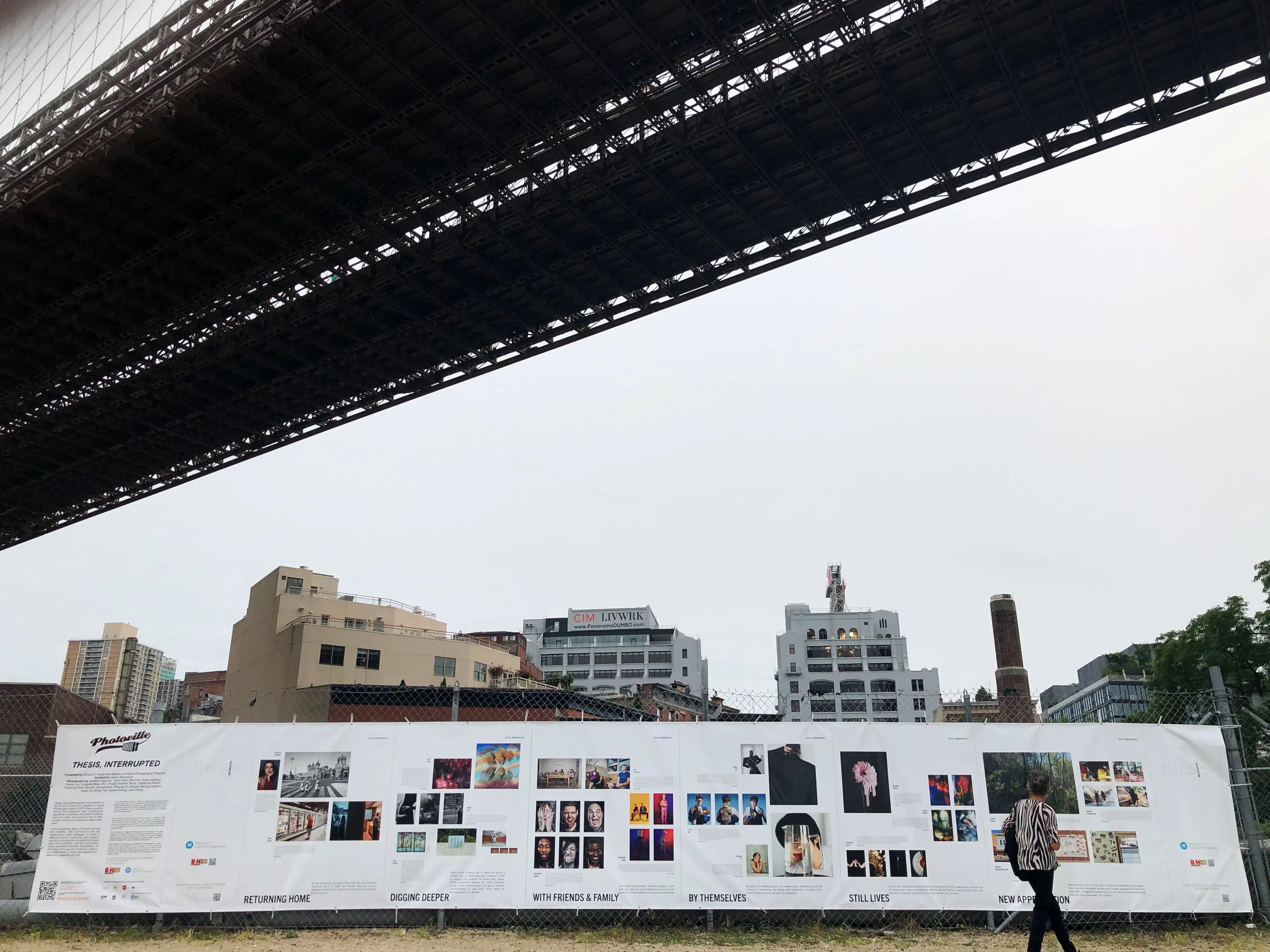 A very long white banner stretches across the lower half of the image, showing photographs by MPS Digital Photography graduates. Overhead is a bridge on an overcast day.