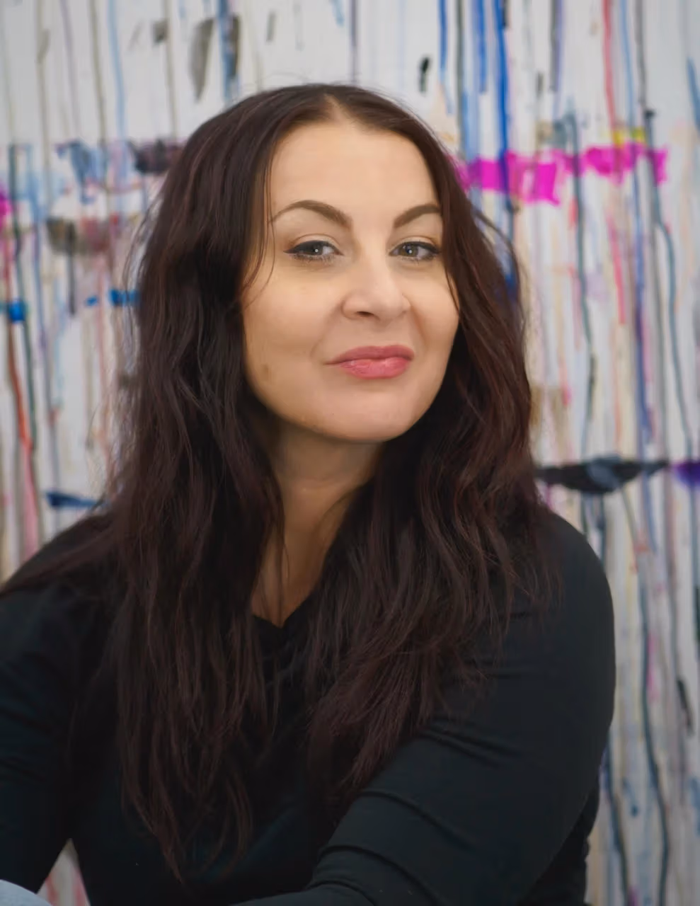portrait of seated woman with long brown hair in front of painted background