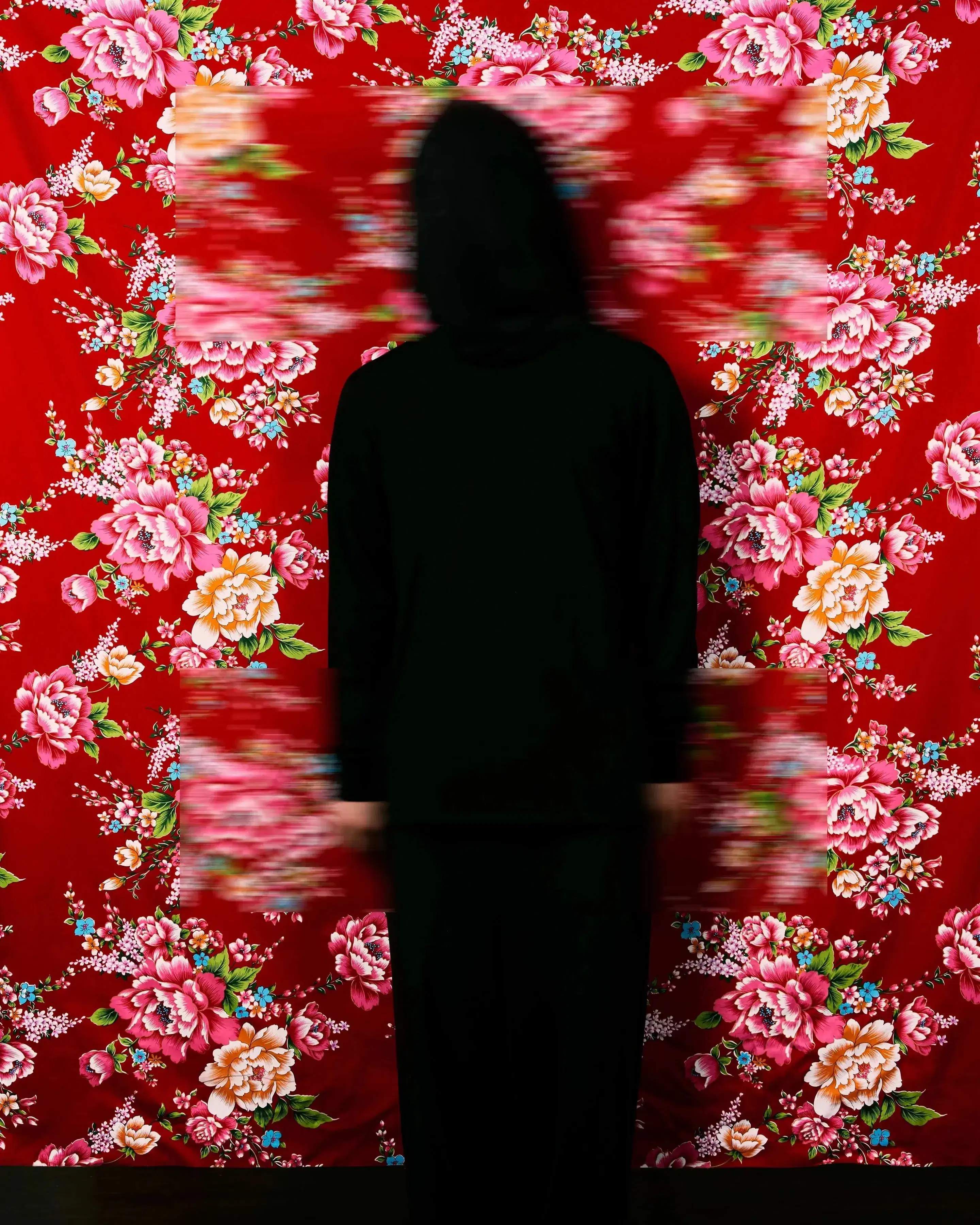 A black silhouette stands in front of a bright red floral wallpaper with two rectangular patches blurred.