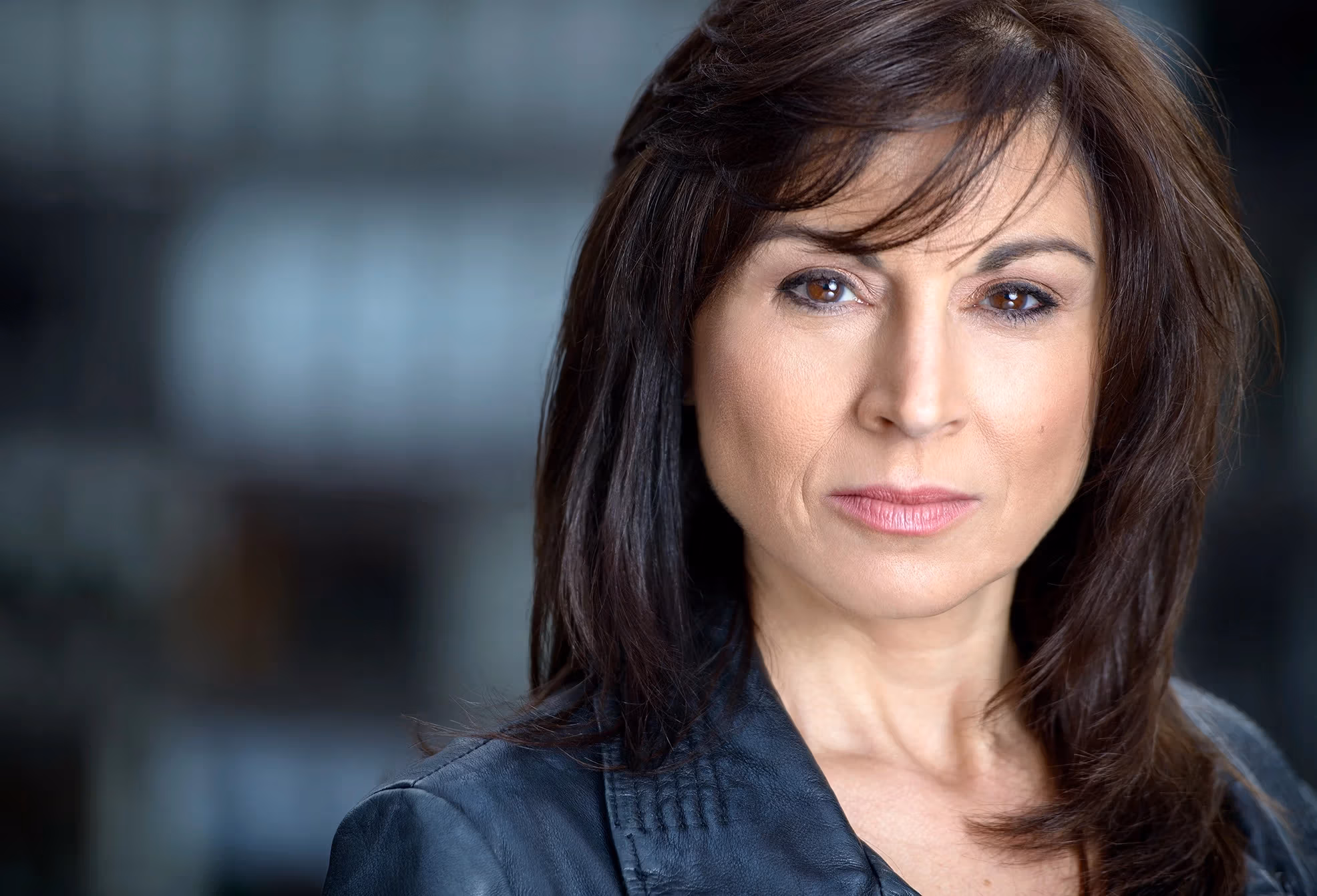 A headshot of a middle aged woman with long brown hair wearing a black jacket.
