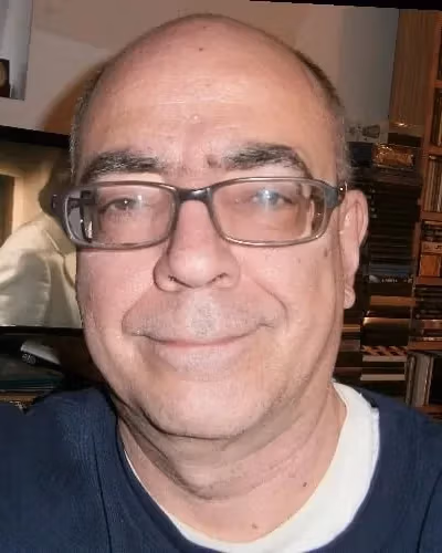 A man in a blue shirt and glasses smiles at the camera