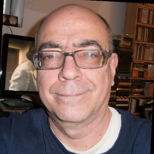 A man in a blue shirt and glasses smiles at the camera